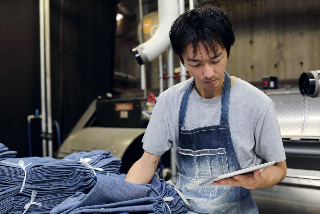 Pemilik konveksi membangun hubungan jangka panjang dengan supplier kain saat memeriksa gulungan denim